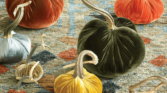 Decorative velvet pumpkins in various colors on a patterned rug.