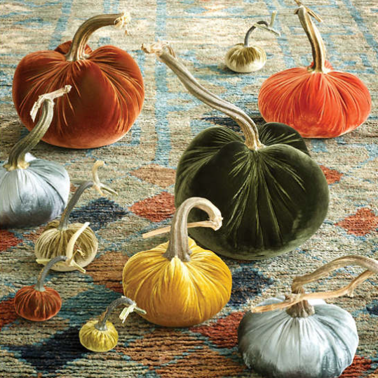 Decorative velvet pumpkins in various colors on a patterned rug.